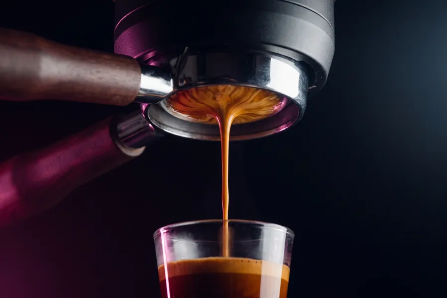 Portafiltro sin fondo extrayendo un espresso en un vaso, con la crema formándose en capas.