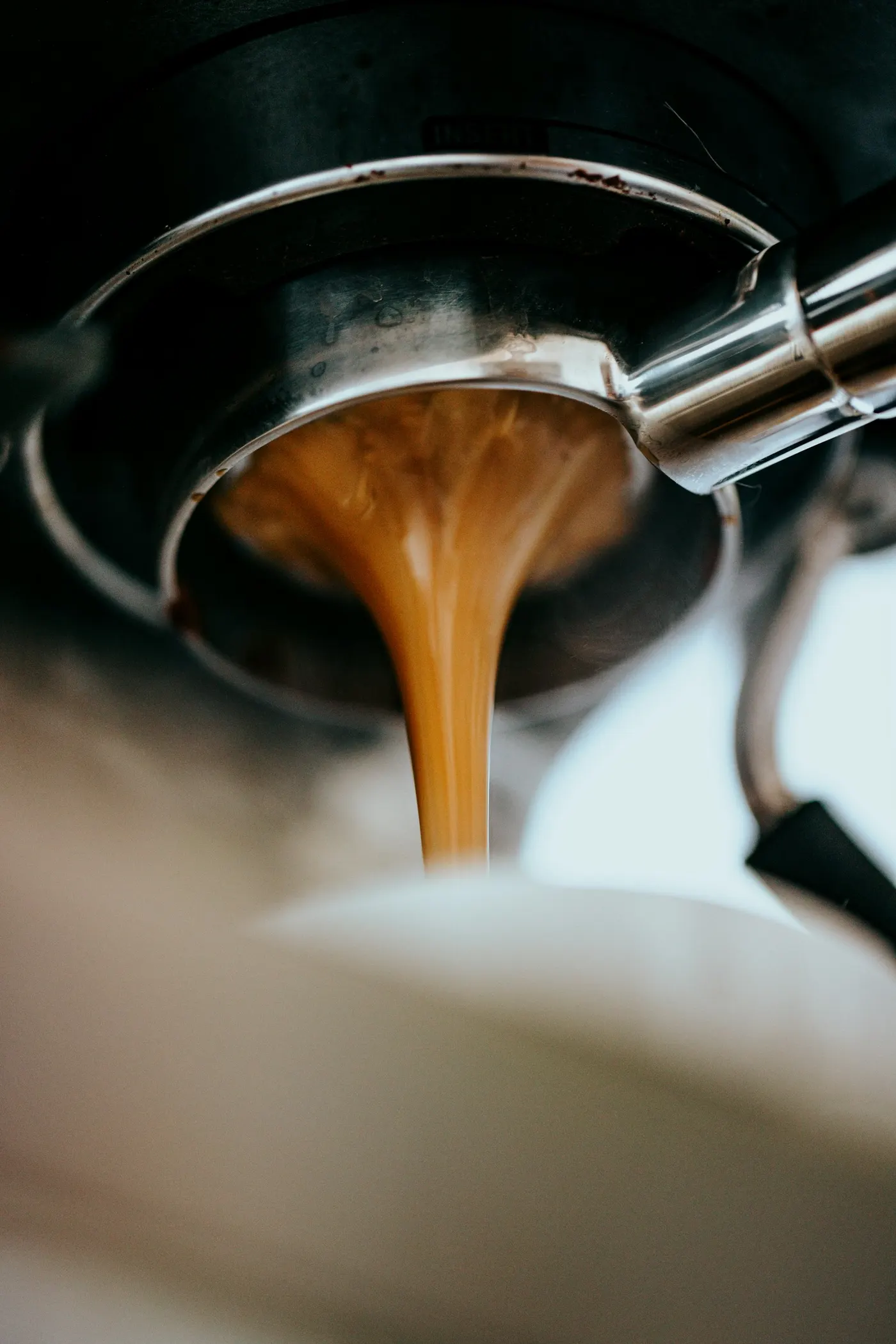 Espresso cayendo en dos hilos desde un portafiltro sin fondo, en primer plano.